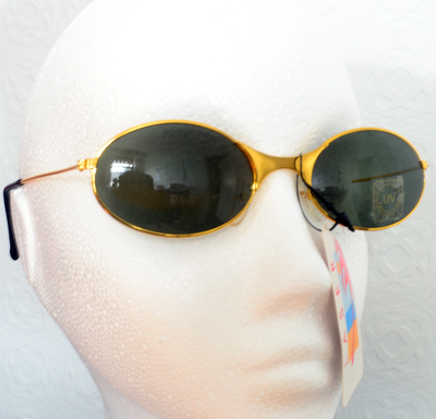 A pair of oval sunglasses with a sleek gold frame and dark lenses is displayed on a white mannequin head.